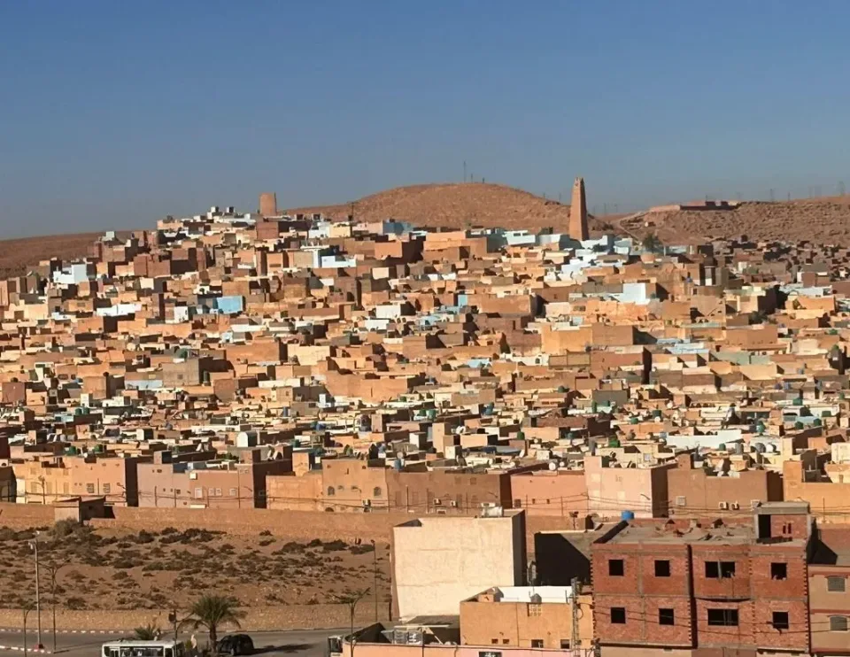 A densely packed desert town in Algeria, featuring traditional mud-brick houses and a minaret against a clear blue sky.